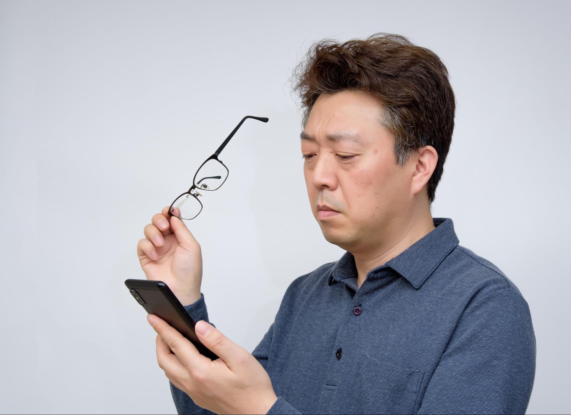 Middle-aged man holding glasses while struggling to read his smartphone, illustrating the meaning of presbyopia.