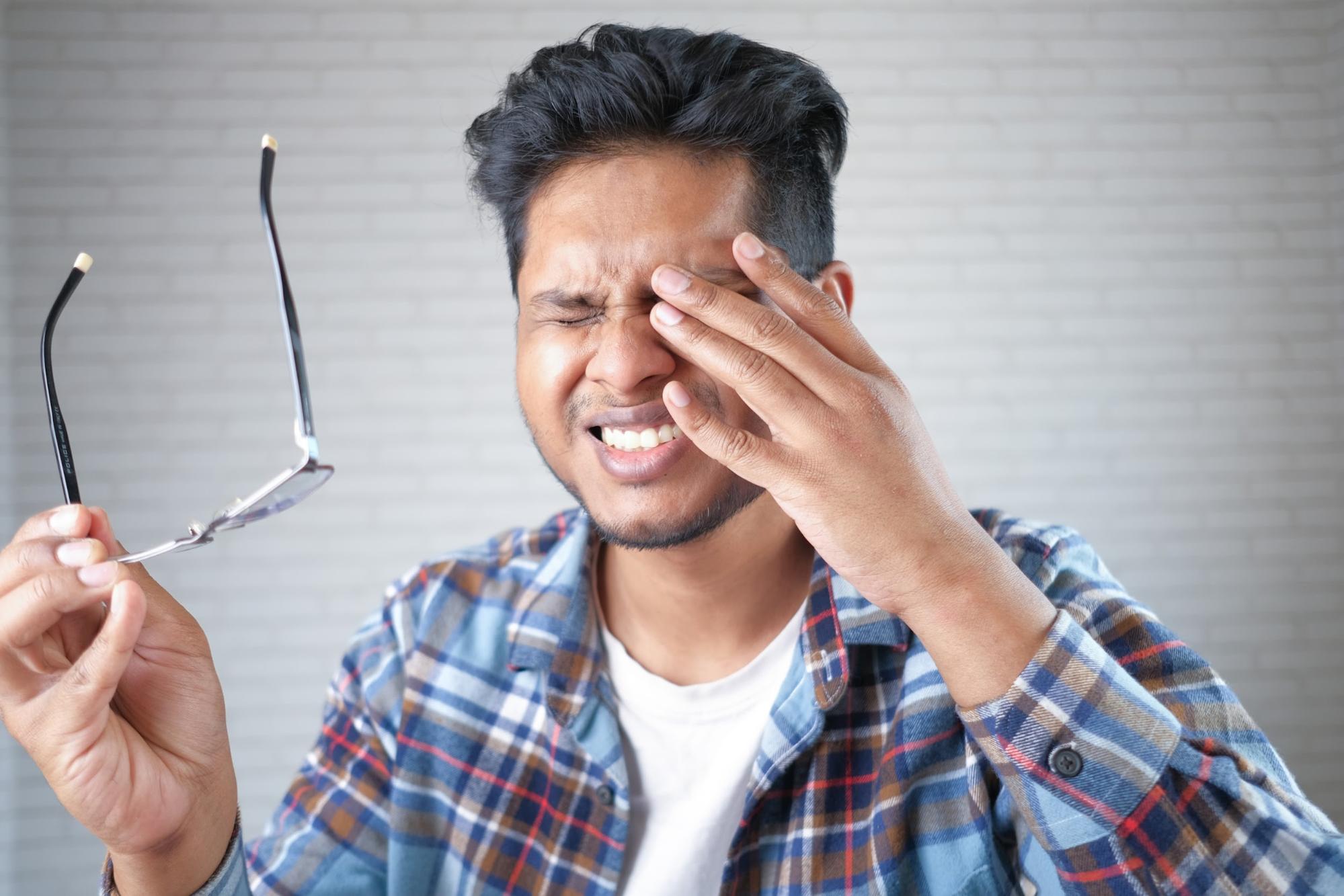 Man holding his eye in discomfort, illustrating symptoms of astigmatism and why understanding what is astigmatism and how can it be corrected matters for eye health.