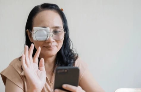 Middle-aged woman with eye patch using smartphone after eye therapy, asking is there a cure for lazy eye in adults