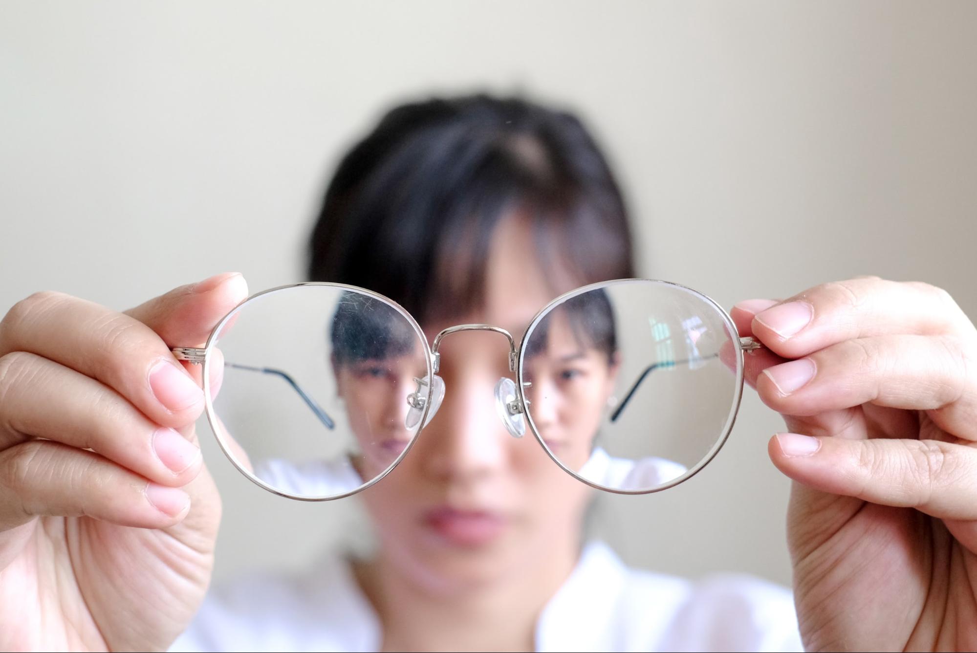 Woman holding eyeglasses highlighting vision distortion exploring refractive lens exchange pros and cons for clearer sight.