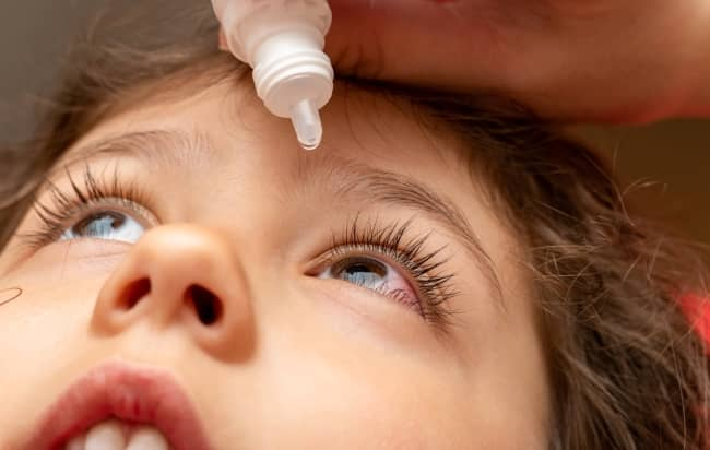 A close-up shows eye drops being administered to a child's eye