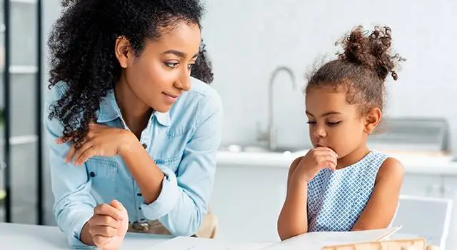 A mother watches her thoughtful young daughter, who looks a bit hesitant, illustrating how amblyopia treatment can affect a child's emotions