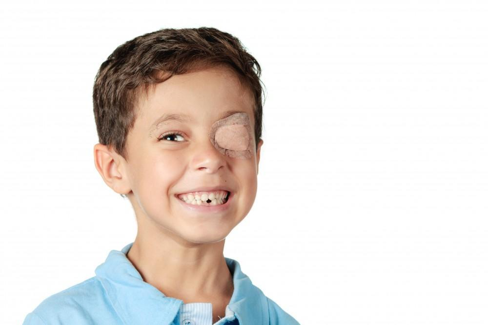 A smiling boy wears an eye patch over one eye, used to treat lazy eye by strengthening the weaker eye