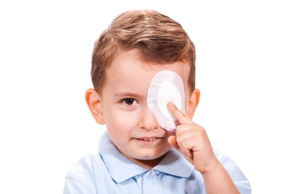 A young boy holds an eye patch over one eye against a plain white background