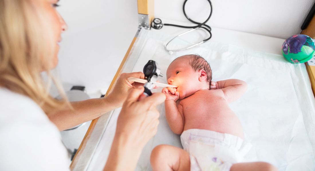 A doctor examines a newborn baby with an otoscope during a checkup