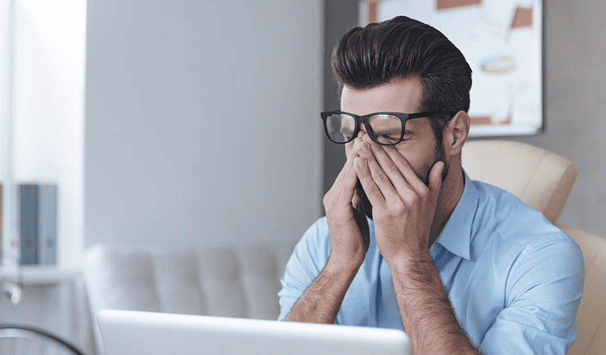 A man rubbing his tired eyes while working at his laptop