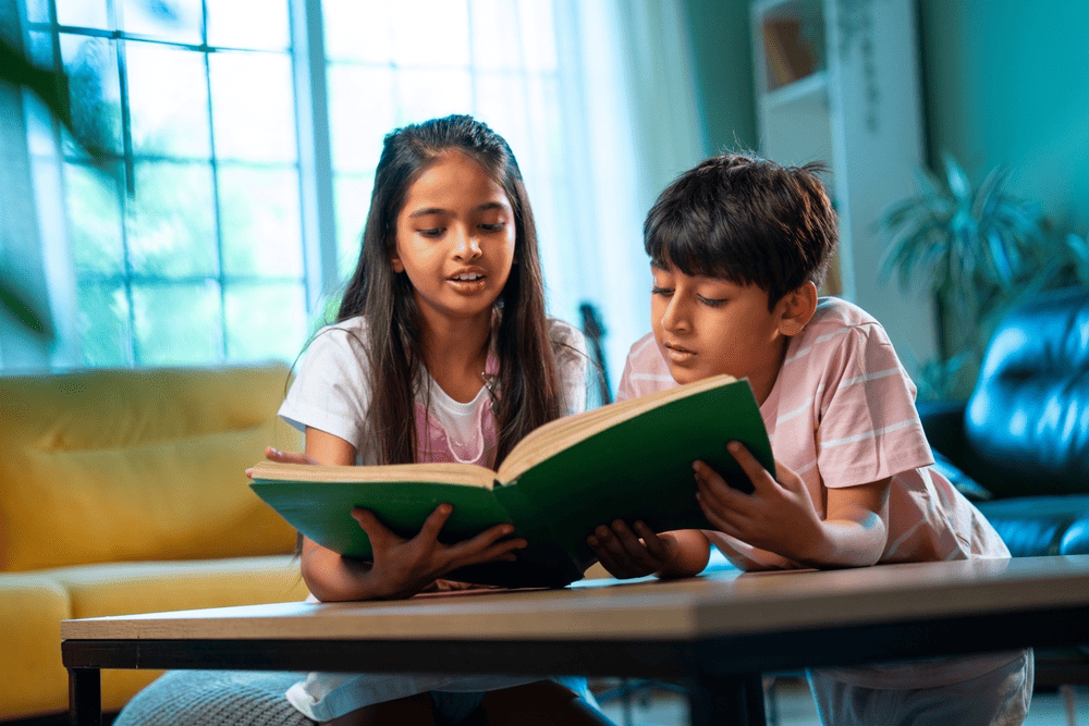 Two children reading a book together at a coffee table