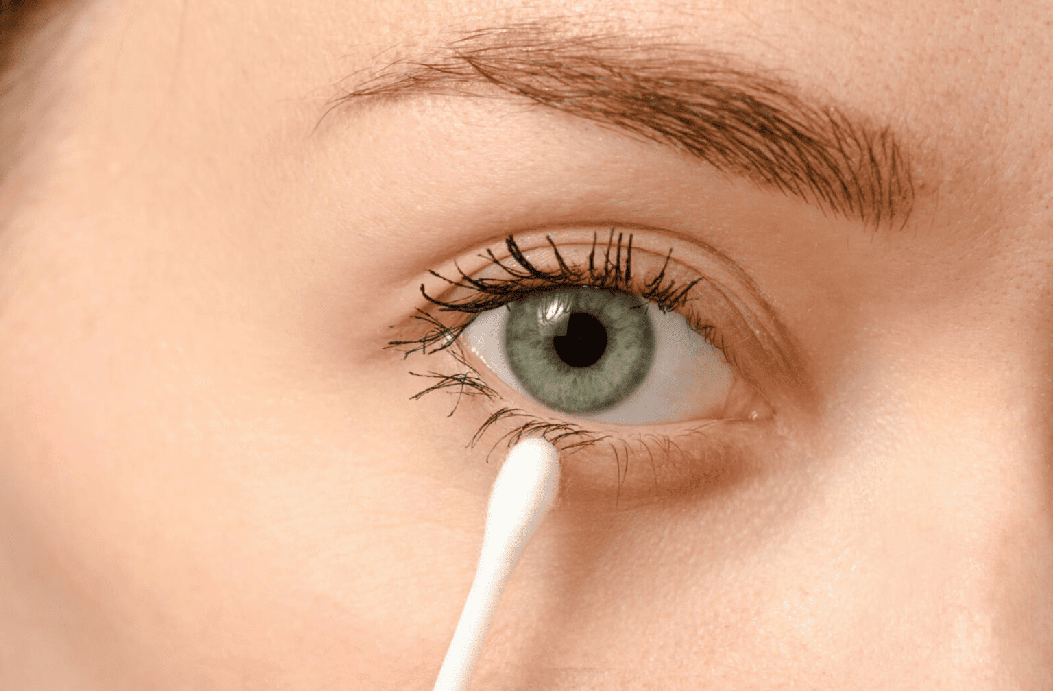 Close-up of a green eye with someone using a white applicator to gently clean the lower eyelid