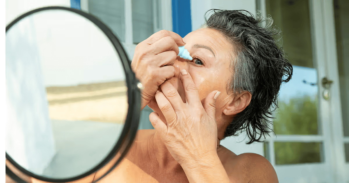 An elderly woman examining their eye in a mirror with their hand pulled down on the lower eyelid