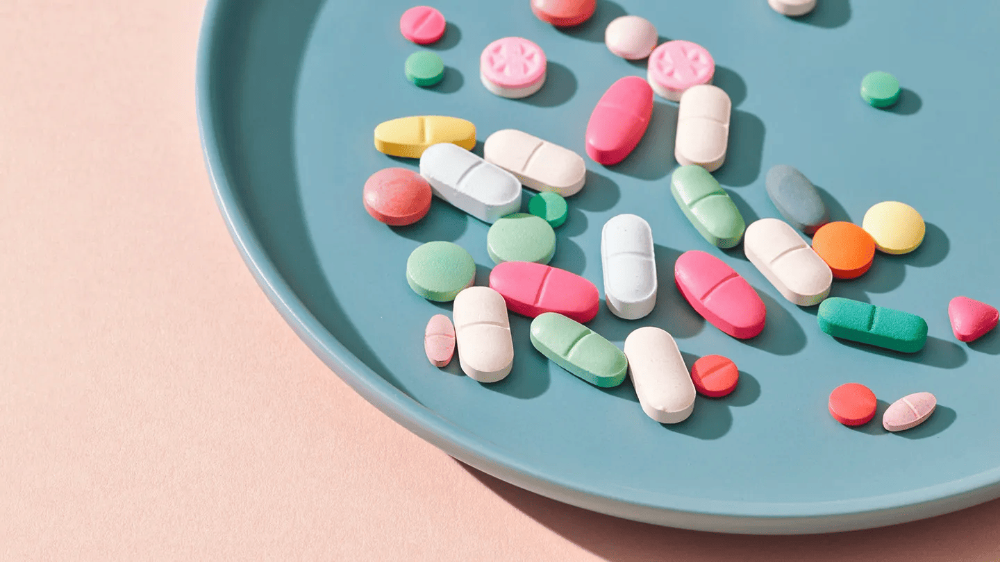 Colorful pills and tablets scattered on a blue plate against a pink background