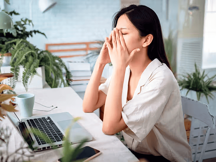 A woman rubbing her tired eyes while working at her laptop