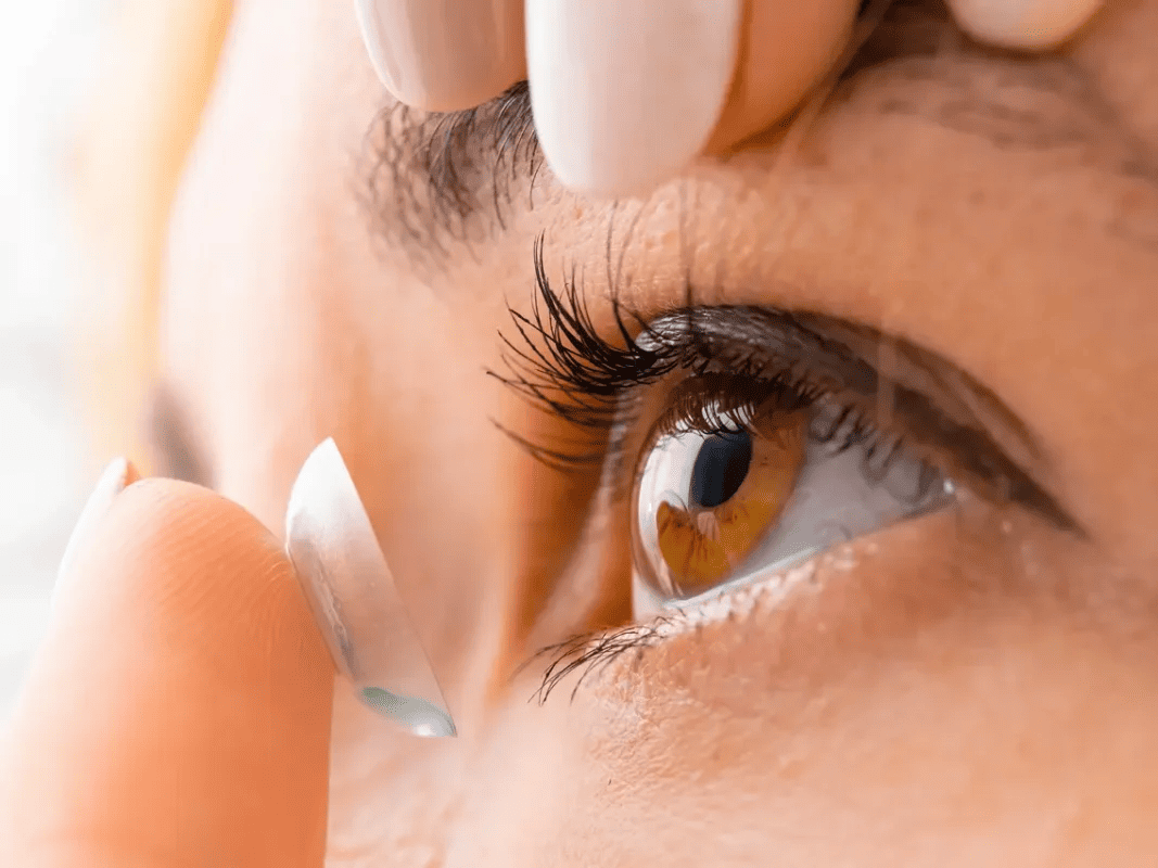 A close-up of a woman inserting a contact lens into her eye