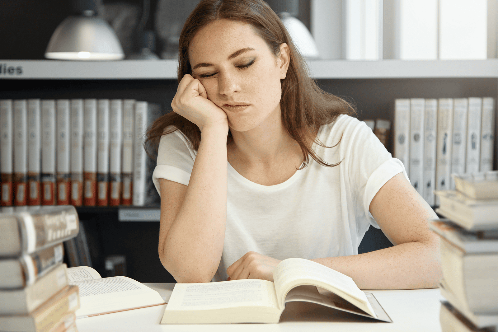 A woman resting her head on her hand while reading a book, looking tired