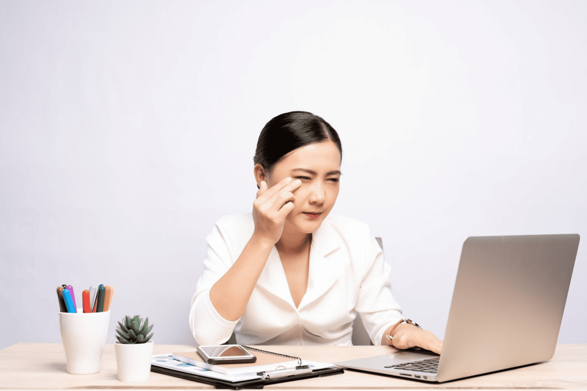 A woman rubbing her eye while working at her laptop