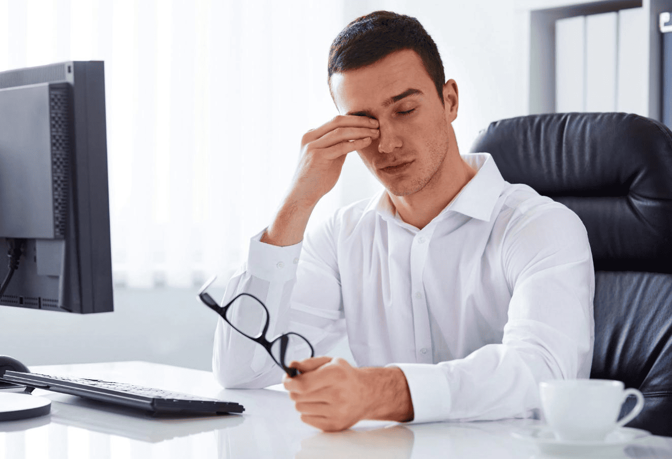 A man rubbing his tired eyes at his office desk