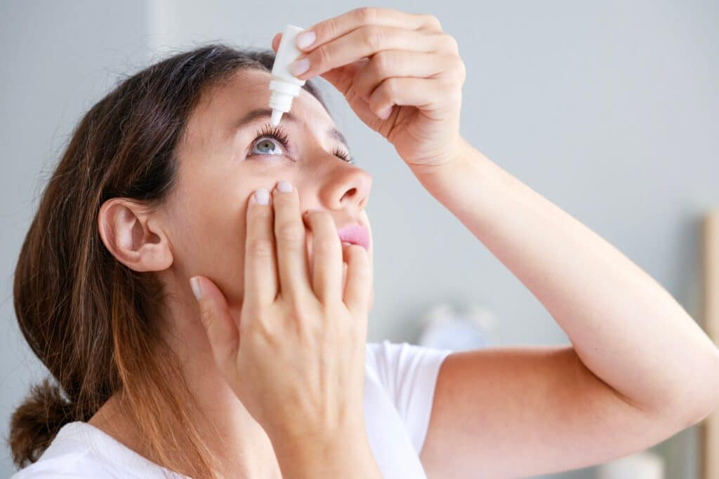 A woman applying eye drops to manage dry eye symptoms.