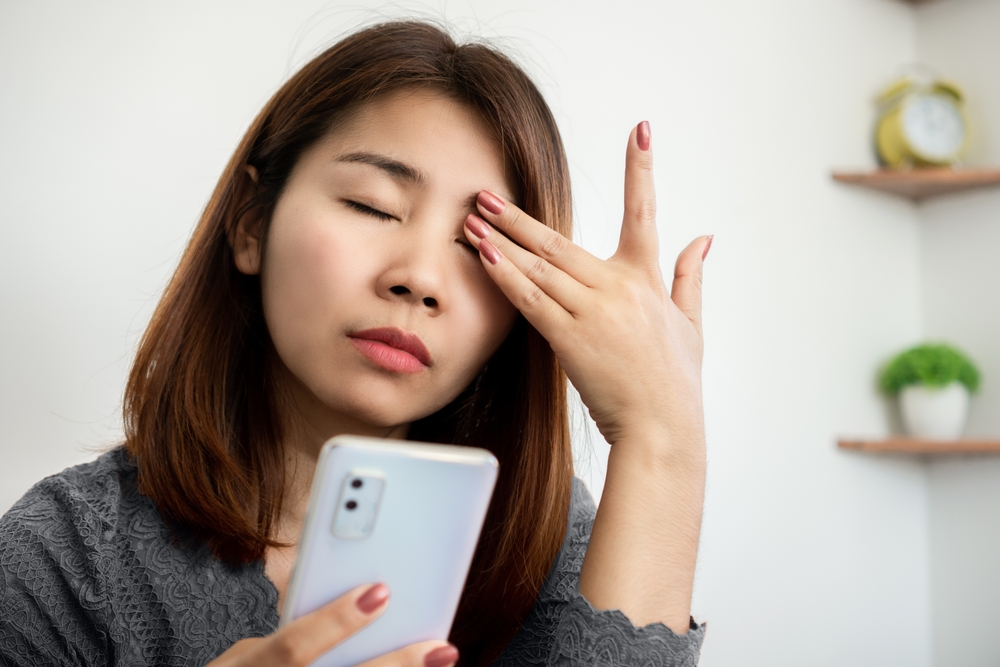 A woman rubbing her eye while looking at her phone